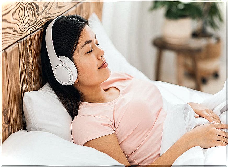 Woman with headphones listening to relaxing music on her bed.